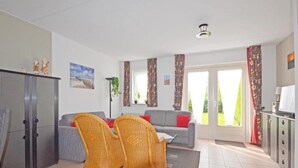 A living room with a sofa, two wicker chairs, a cabinet, and a window with curtains. - Bungalow in Breskens Near the Beach (Breskens)