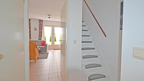 A staircase with a handrail, a living room with a sofa and a window, and a tiled floor. - Bungalow in Breskens Near the Beach (Breskens)