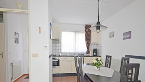 A compact kitchen with a dining table and chairs, a window with curtains, and a radiator. - Bungalow in Breskens Near the Beach (Breskens)