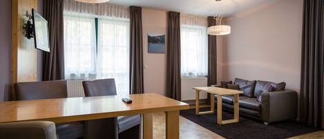 A modern living room with a wooden dining table, two sofas, and a TV mounted on the wall.