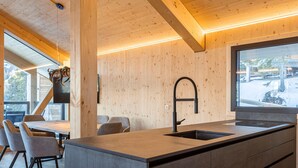 A modern kitchen with a large island, wooden walls, and a large window. - Charming Chalet With hot tub and Sauna (Stadl-Predlitz)