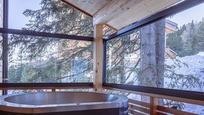 A modern bathroom with a large bathtub, wooden slatted walls, and a view of a snowy forest. - Charming Chalet With hot tub and Sauna (Stadl-Predlitz)