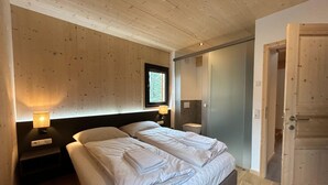 A bedroom with a wooden ceiling, a bed with white linens, bedside lamps, and a window with a view. - Charming Chalet With hot tub and Sauna (Stadl-Predlitz)