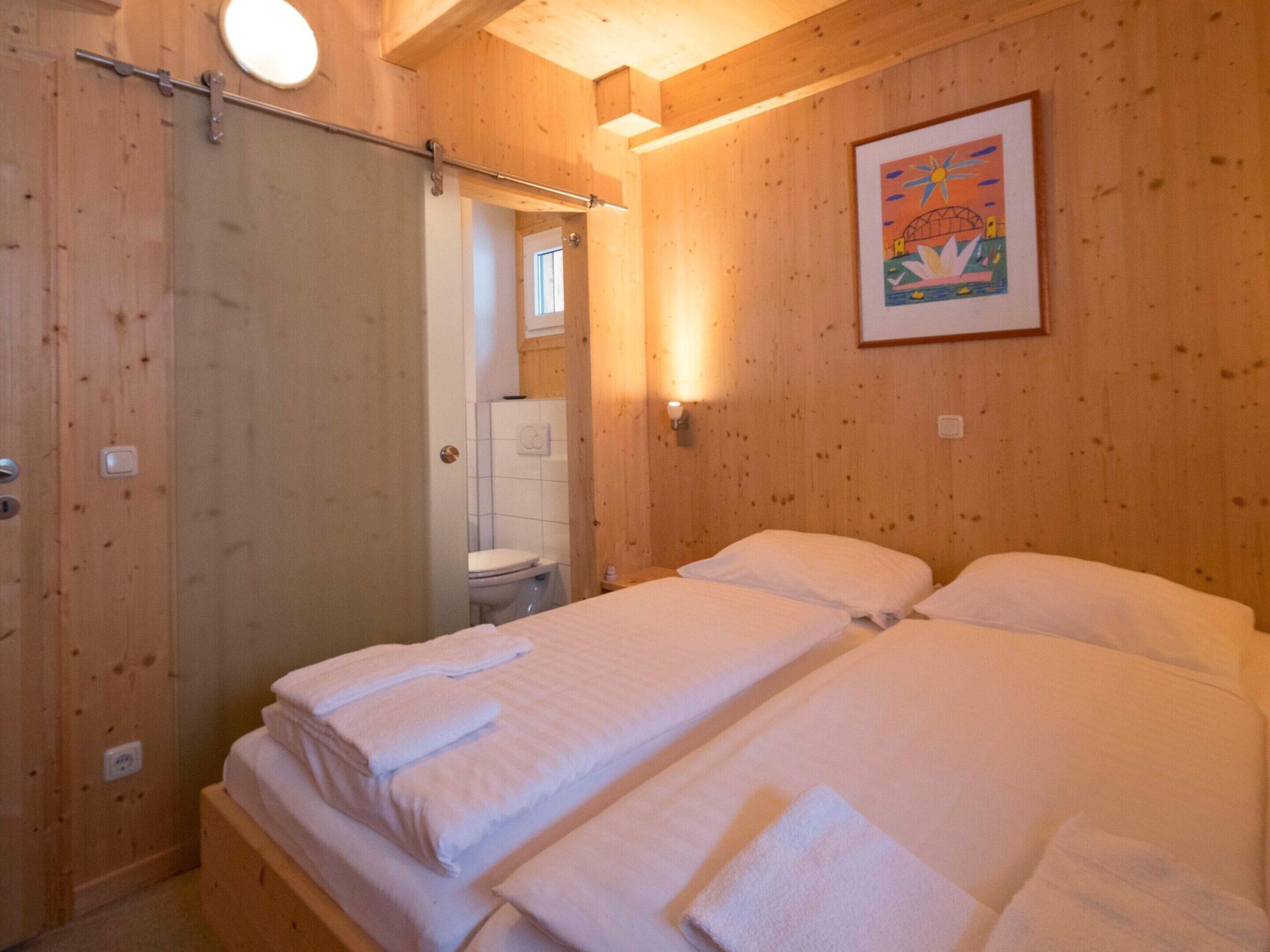 Ein Zimmer mit Holzboden, zwei Betten, einem Badezimmer und einer Tür.