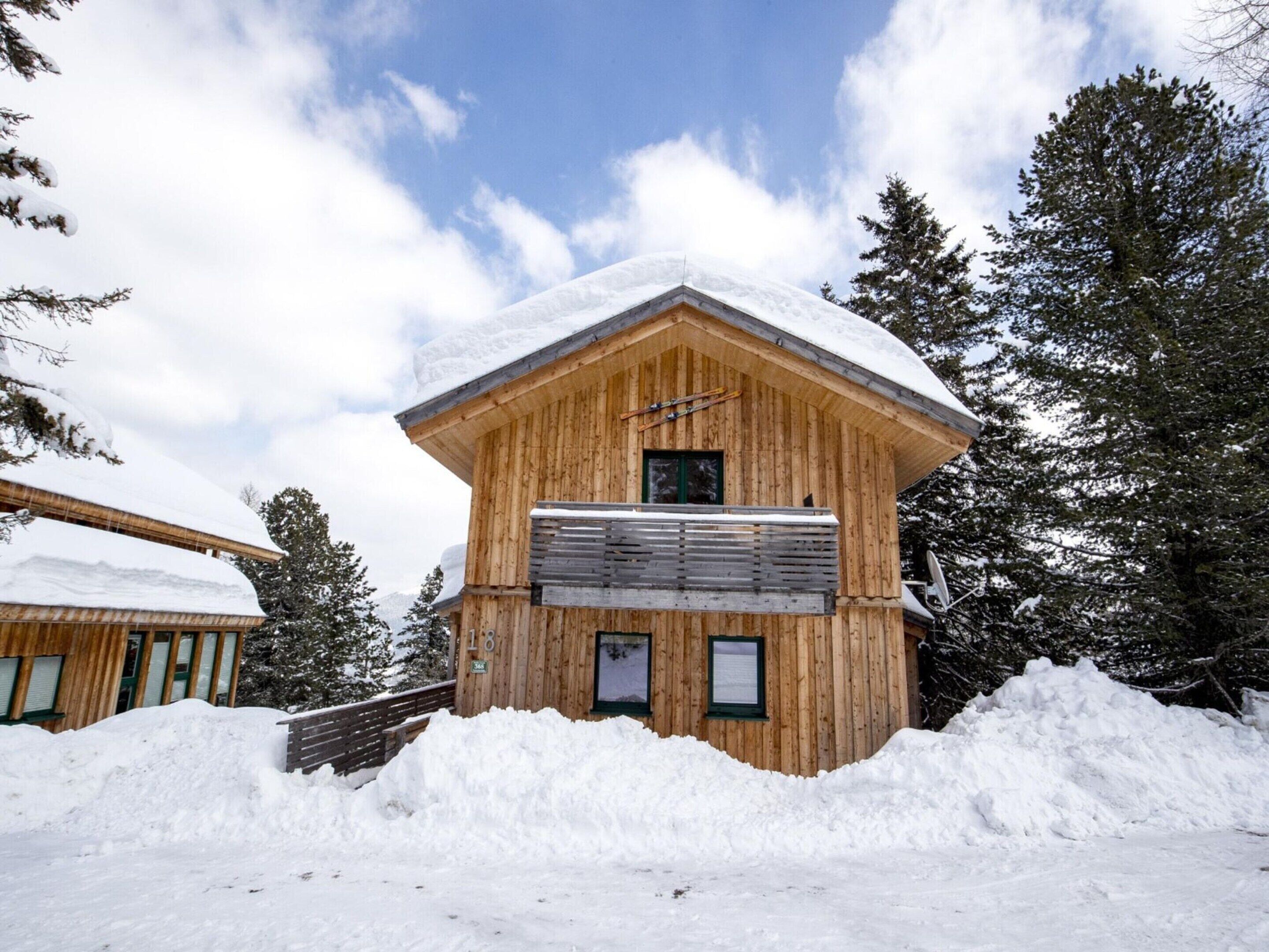 A wooden chalet with a sloped roof, surrounded by snow and trees.