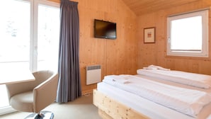 En stuga med träpanel, inredd med en säng, en tv, en stol och ett fönster med gardiner.