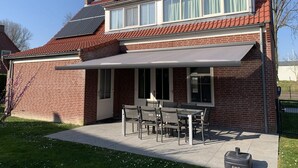 A two-story brick house with a red-tiled roof, a covered patio with a table and chairs, and a large window with white curtains. - House in Netherlands for 8 With Modern Comfort (Breskens)