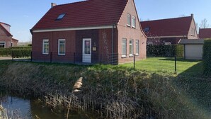 A single-story brick house with a red-tiled roof, a small front yard, and a body of water in front. - House in Netherlands for 8 With Modern Comfort (Breskens)