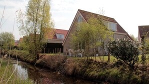 A residential house with a sloped roof, a small garden, and a stream in the foreground.