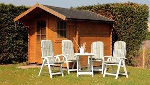 A wooden cabin with a sloped roof, a small table with chairs, and a window.