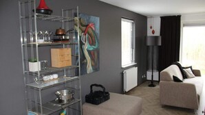 A hotel room with a kitchenette, a sofa, a painting, and a window with blinds.