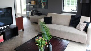 A modern living room with a sofa, a coffee table with flowers, a TV, a bookshelf, and a painting on the wall.