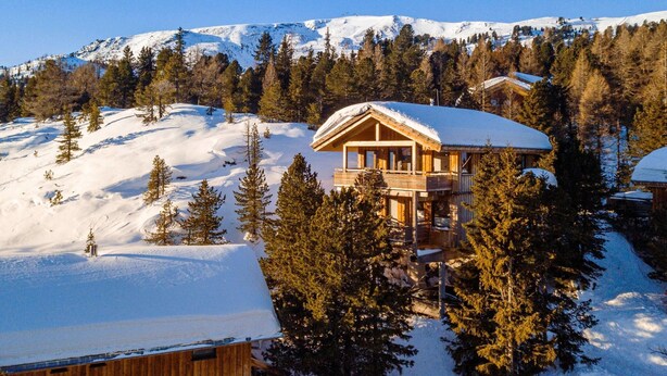 Een houten chalet met een balkon, omgeven door met sneeuw bedekte bomen en bergen op de achtergrond.