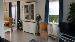 A living room with a dining area, a white cabinet with glass doors, a television, and a potted plant. - Bungalow in Breskens Near Beach and Sea (Breskens)