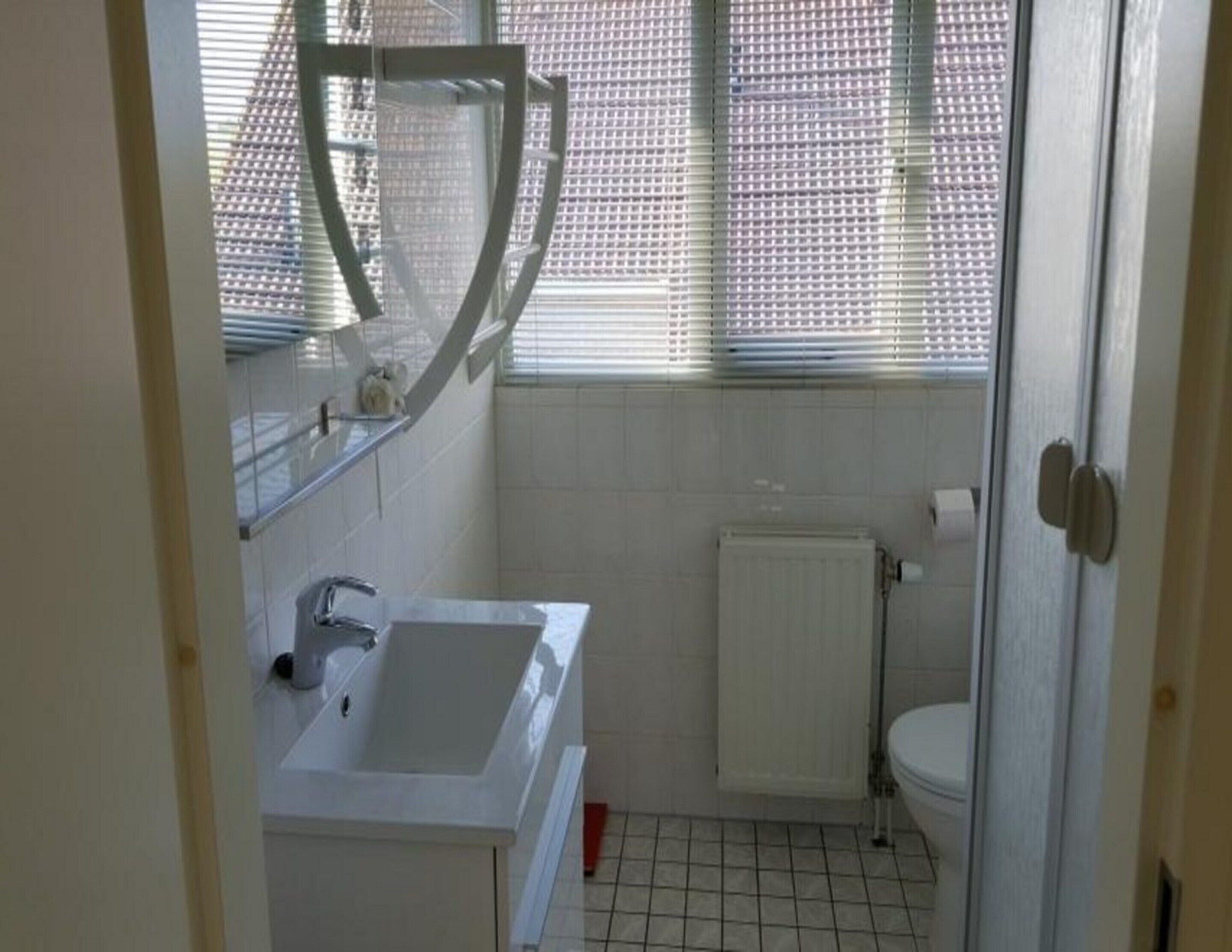 Kylpyhuoneessa on valkoinen pesuallas, wc ja ikkuna, jossa on sälekaihtimet.