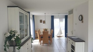 A compact kitchen with white cabinets, a dining area with a wooden table and chairs, and a small sailboat decoration. - Bungalow in Breskens Near Beach and Sea (Breskens)