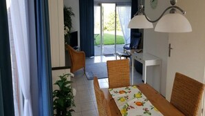 A dining area with a table set for four, a television, and a view of a garden through a glass door. - Bungalow in Breskens Near Beach and Sea (Breskens)