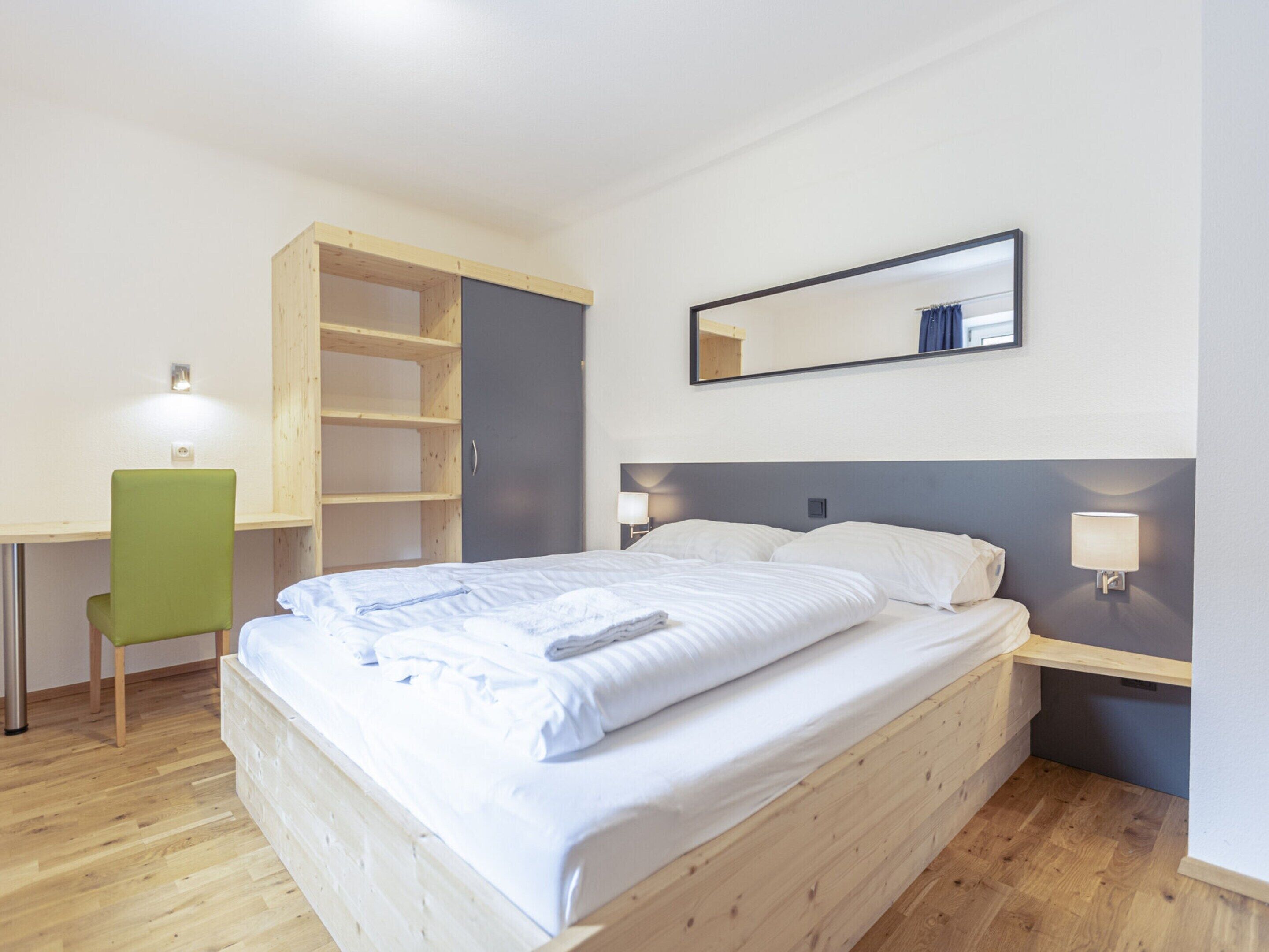 A bedroom with a bed, a desk, a chair, a wardrobe, and a mirror.