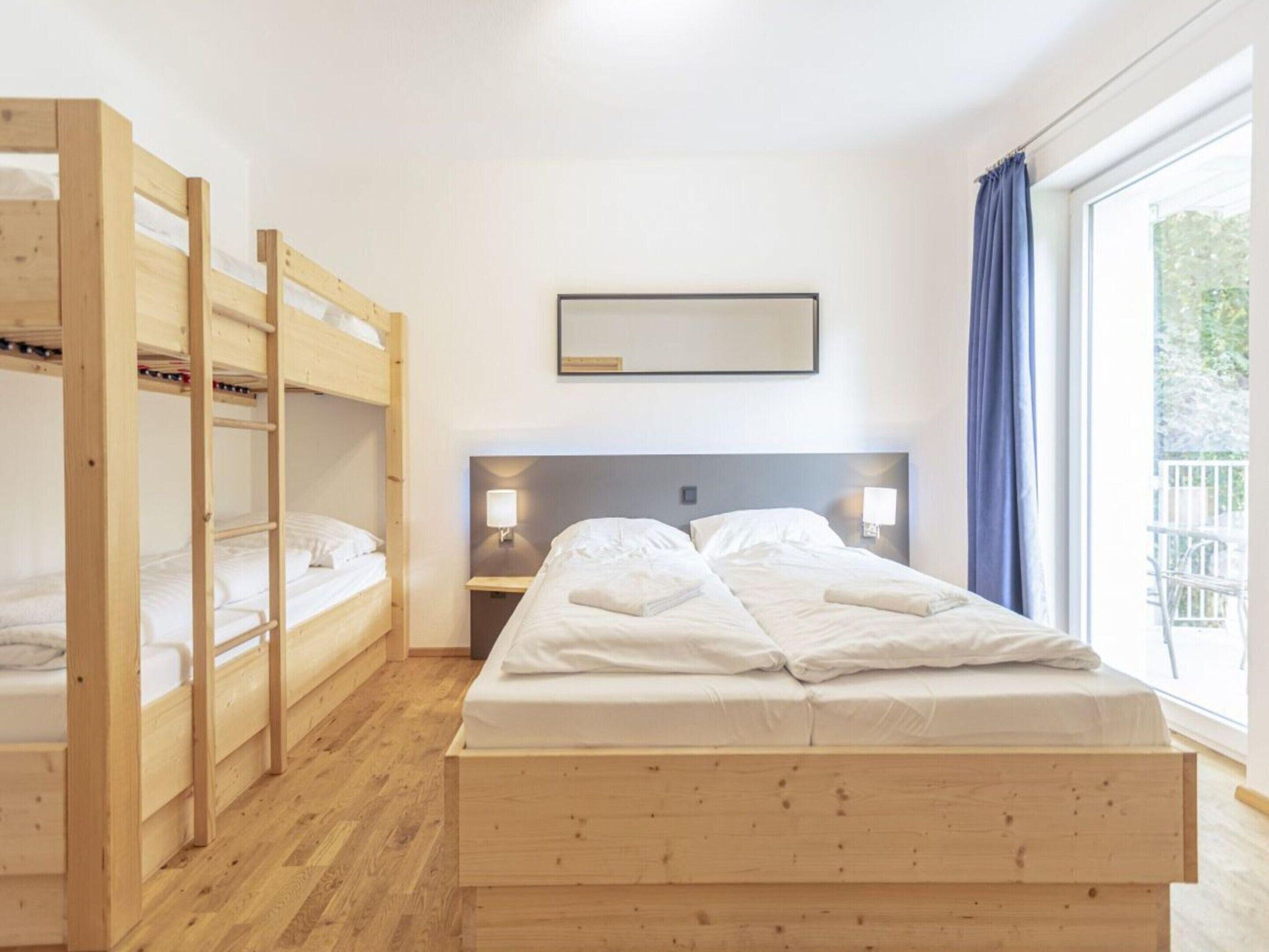 Ein Zimmer mit einem großen Bett, Holzbettställen, einem Nachttisch mit Lampe und einem Fenster mit Vorhängen.