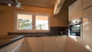 Una cocina moderna con armarios de madera, un horno de acero inoxidable y una ventana con vista a árboles.