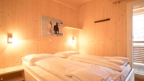 Una habitación con una cama, paredes de madera, un cuadro y una ventana con persianas.