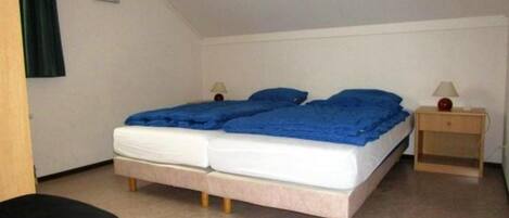 A single bed with a blue blanket, a bedside table with a lamp, and a chair.