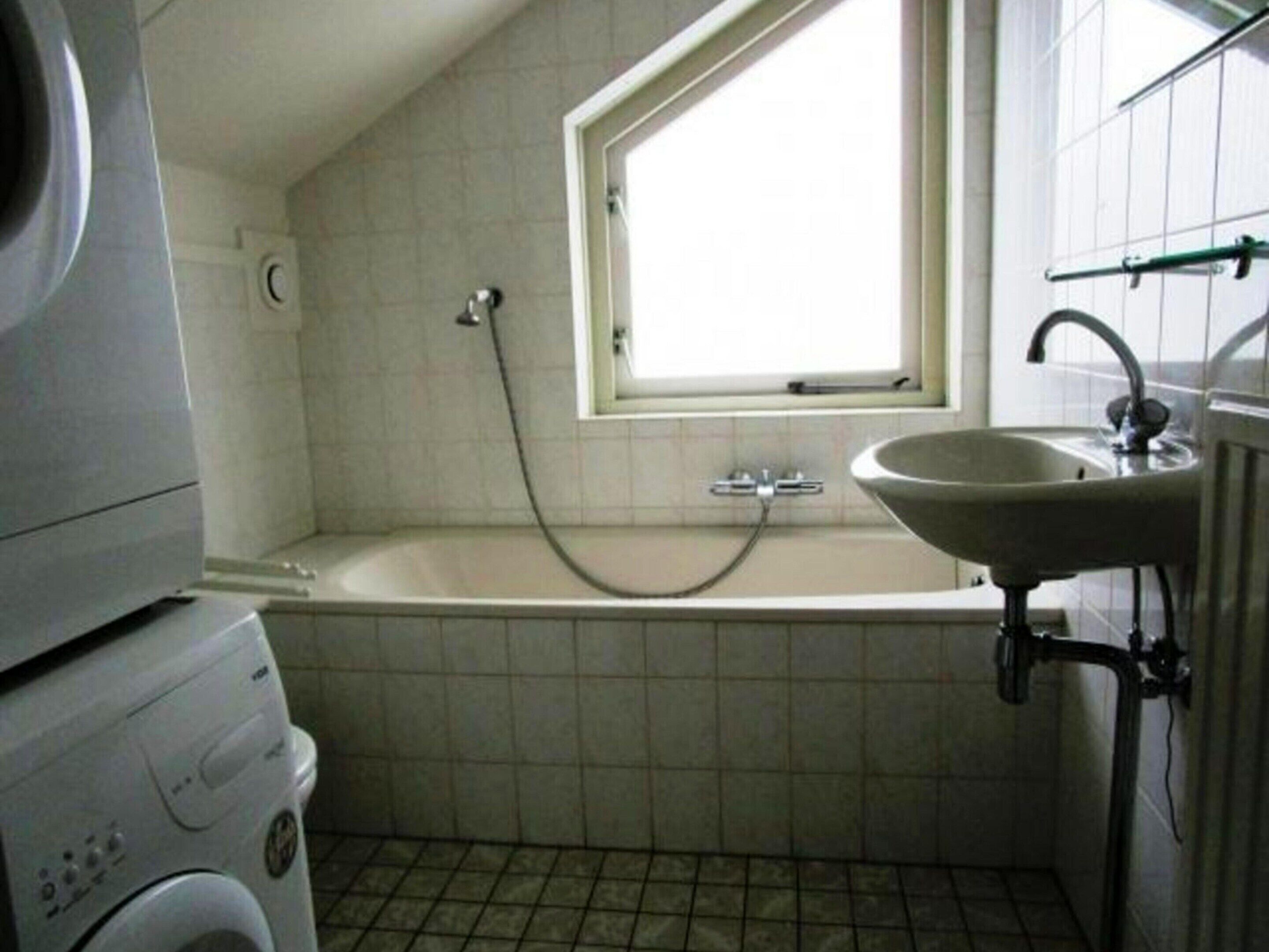 Een badkamer met een badkuip, een raam, een wastafel en een wasmachine.