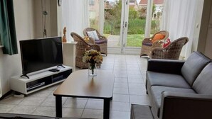 A living room with a sofa, a coffee table, a TV, and wicker chairs. - Bungalow in Breskens Near Beach and Pool (Breskens)