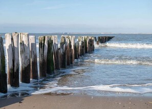 A beach with wooden posts extending into the water, a sandy shore, and waves gently breaking on the beach. - Family Retreat in Breskens (Breskens)