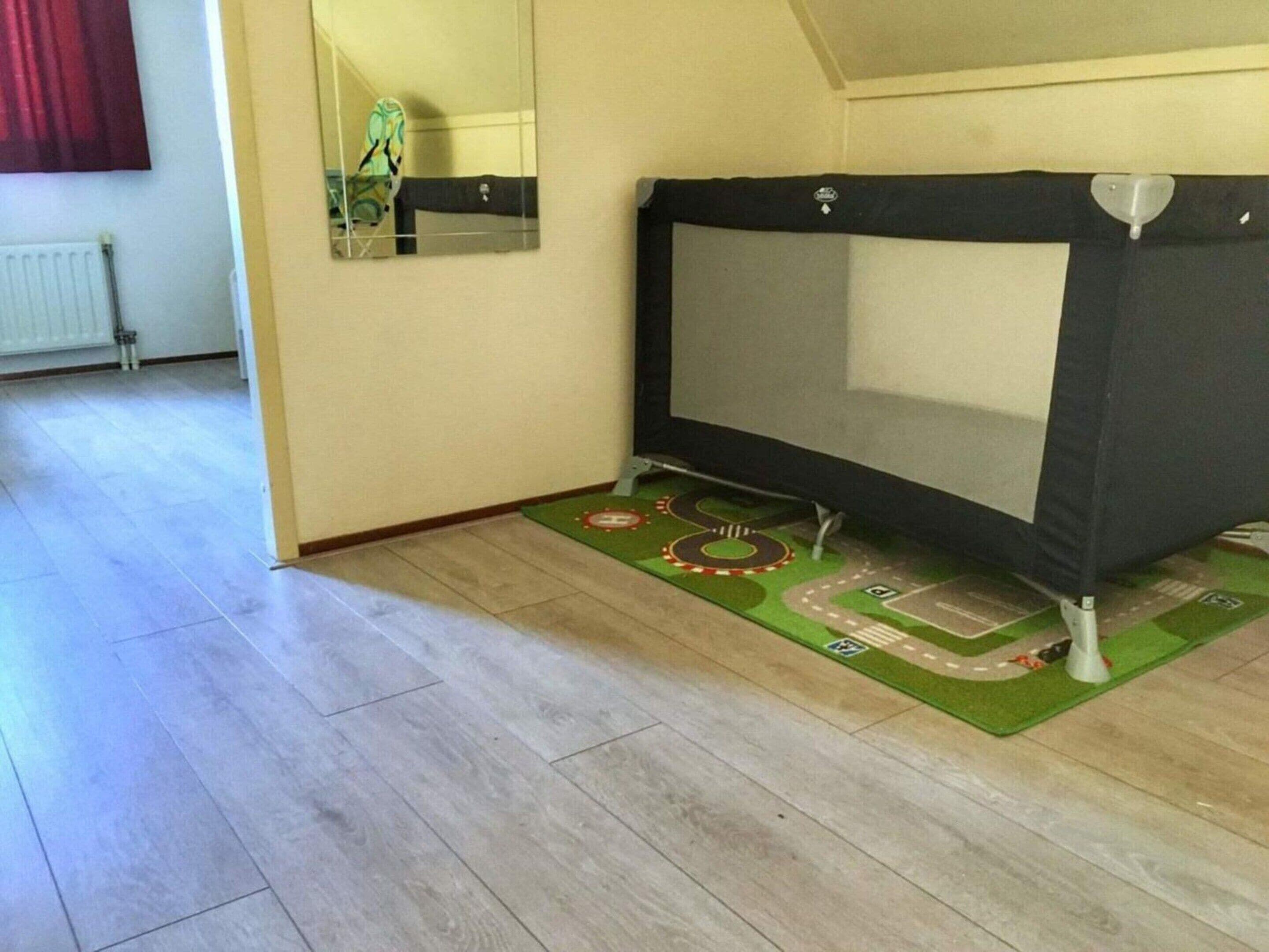 A room with a bed, a mirror, a radiator, and a green mat with road designs.
