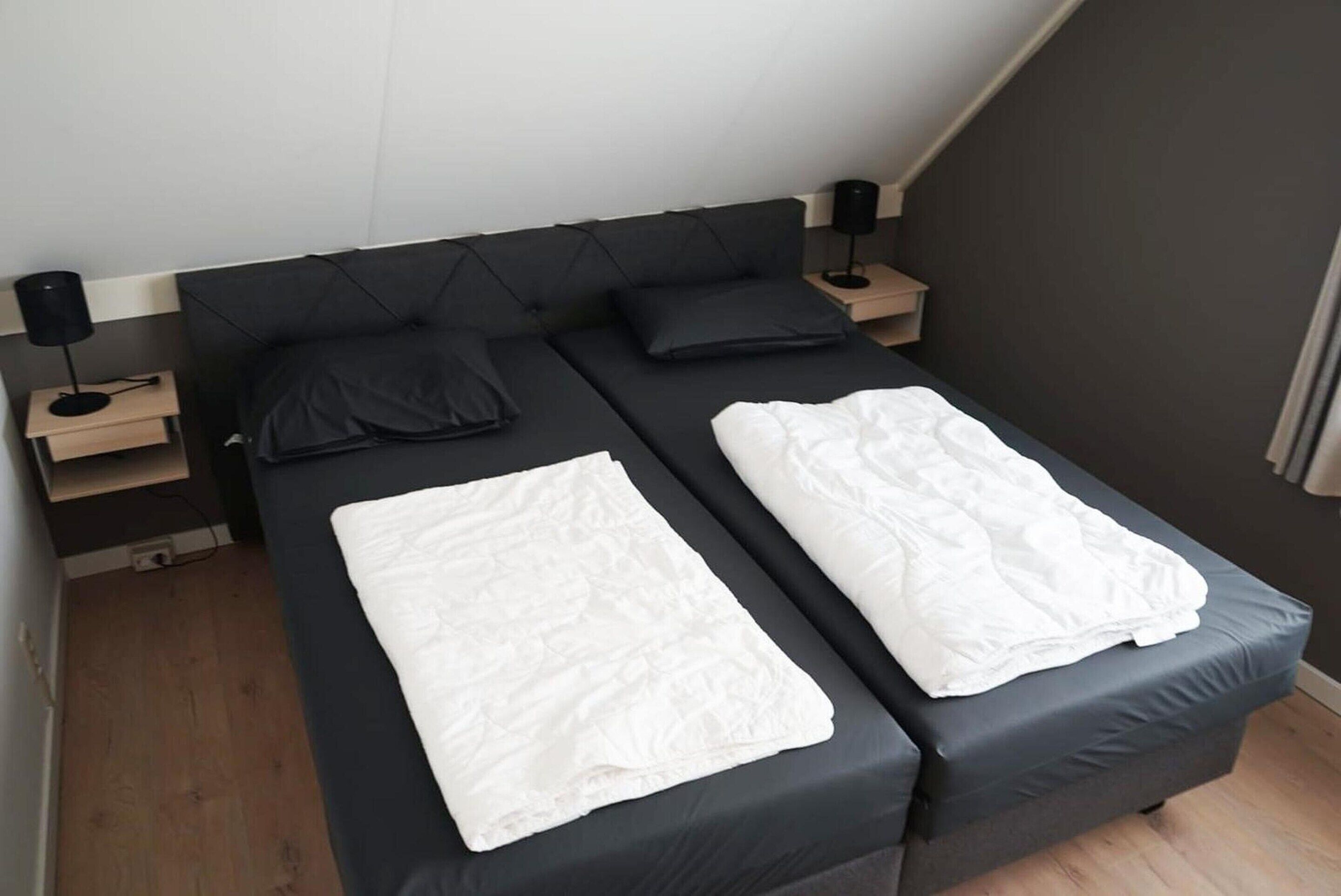 A twin bed with a dark headboard, two bedside tables with lamps, and a wooden floor.
