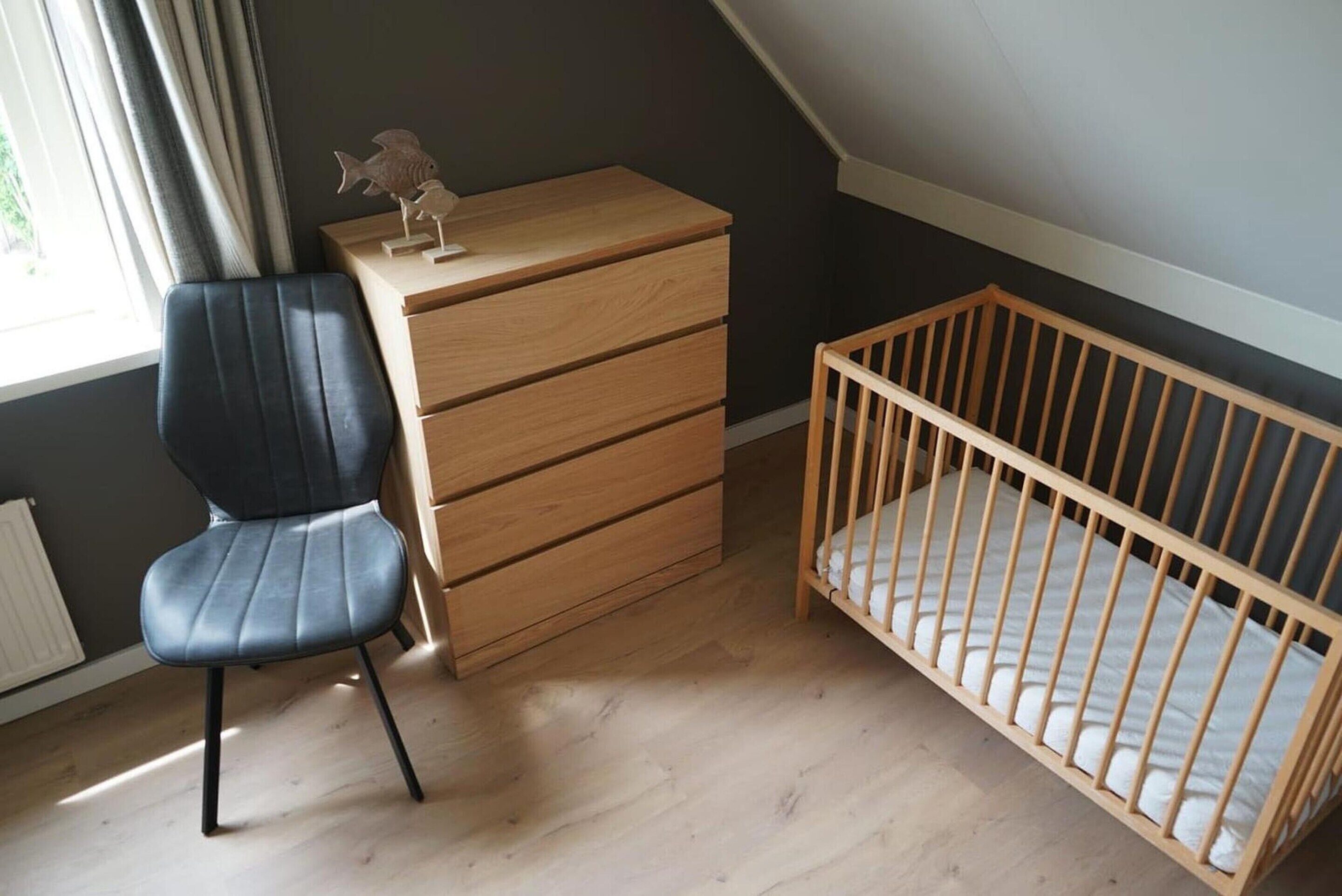 A room with a wooden crib, a desk with drawers, a chair, and a radiator.