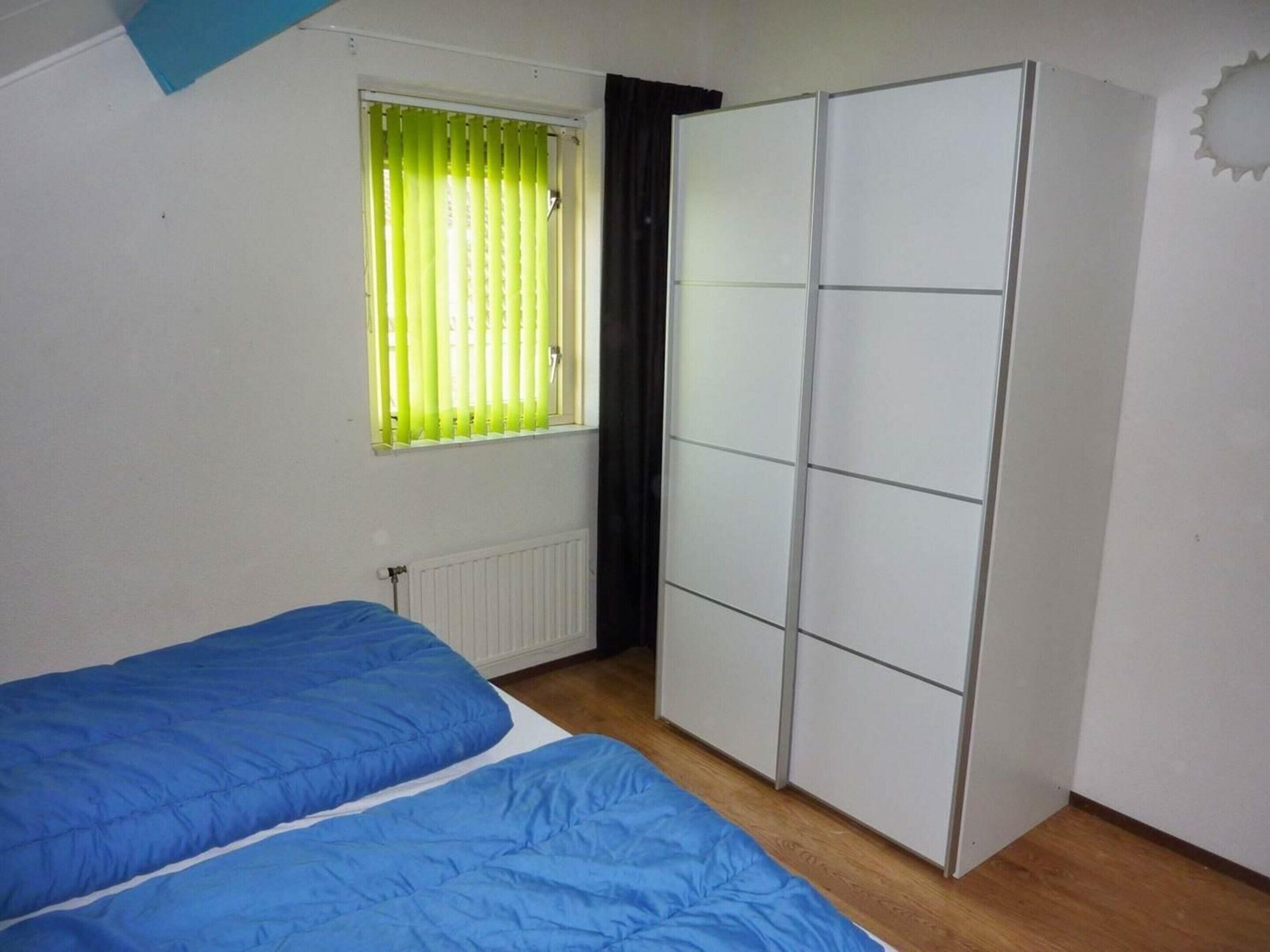 A room with two beds, a radiator, a window with blinds, and a wardrobe.