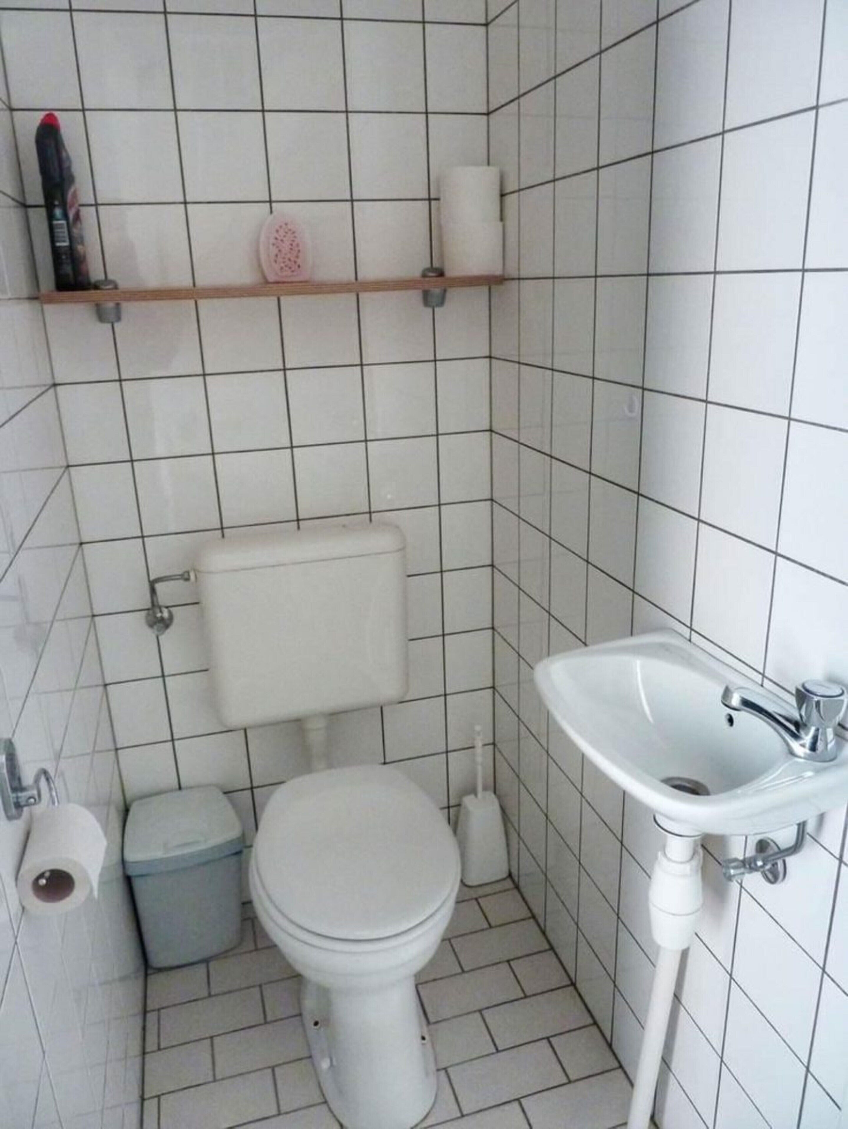 A small, tiled bathroom with a toilet, a sink, and a trash bin.