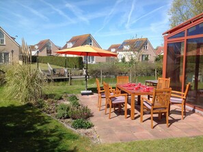Eine Terrasse mit Tisch und Stühlen, ein kleiner Garten und Blick auf benachbarte Häuser.