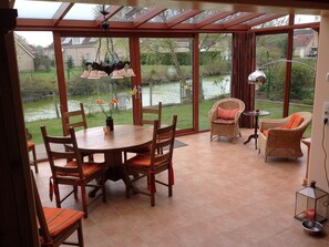 Ein Wintergarten mit Esstisch, Stühlen, Korbmöbeln und Blick auf einen See.