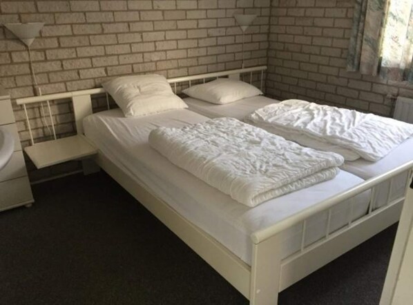 Une chambre avec un lit simple, une table de chevet blanche et un mur en briques.