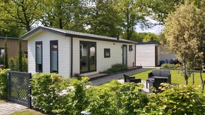 A single-story mobile home with a patio area, surrounded by greenery and trees. - House in Breskens Near the Beach (Breskens)