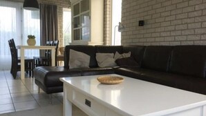 A modern living room with a black leather sofa, a white coffee table, and a dining area with a table and chairs. - House in Breskens Near the Beach (Breskens)