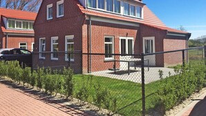 Ett tvåvåningshus byggt av tegel med ett rött tegeltak, en inhägnad trädgård och en asfalterad uppfart.