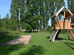 A wooden play structure with a slide and climbing area, surrounded by a grassy field and trees. - Holiday Home Breskens Near the Coast (Breskens)