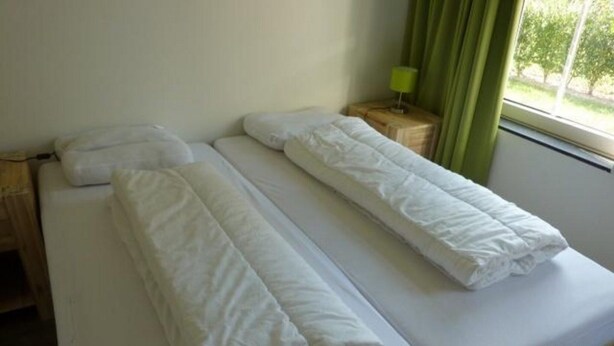 Una cama doble con ropa de cama blanca, una mesita de noche con lámpara y una ventana con cortinas.
