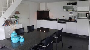 A modern kitchen with white cabinets, a black countertop, and a dining area with a glass table and black chairs. - Cozy House in Breskens Near Scenic Beaches (Breskens)