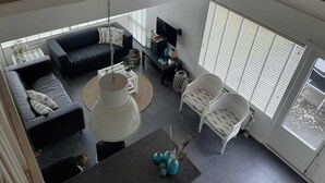 A spacious living area with a black sofa, white chairs, a round coffee table, and a large window with blinds. - Cozy House in Breskens Near Scenic Beaches (Breskens)