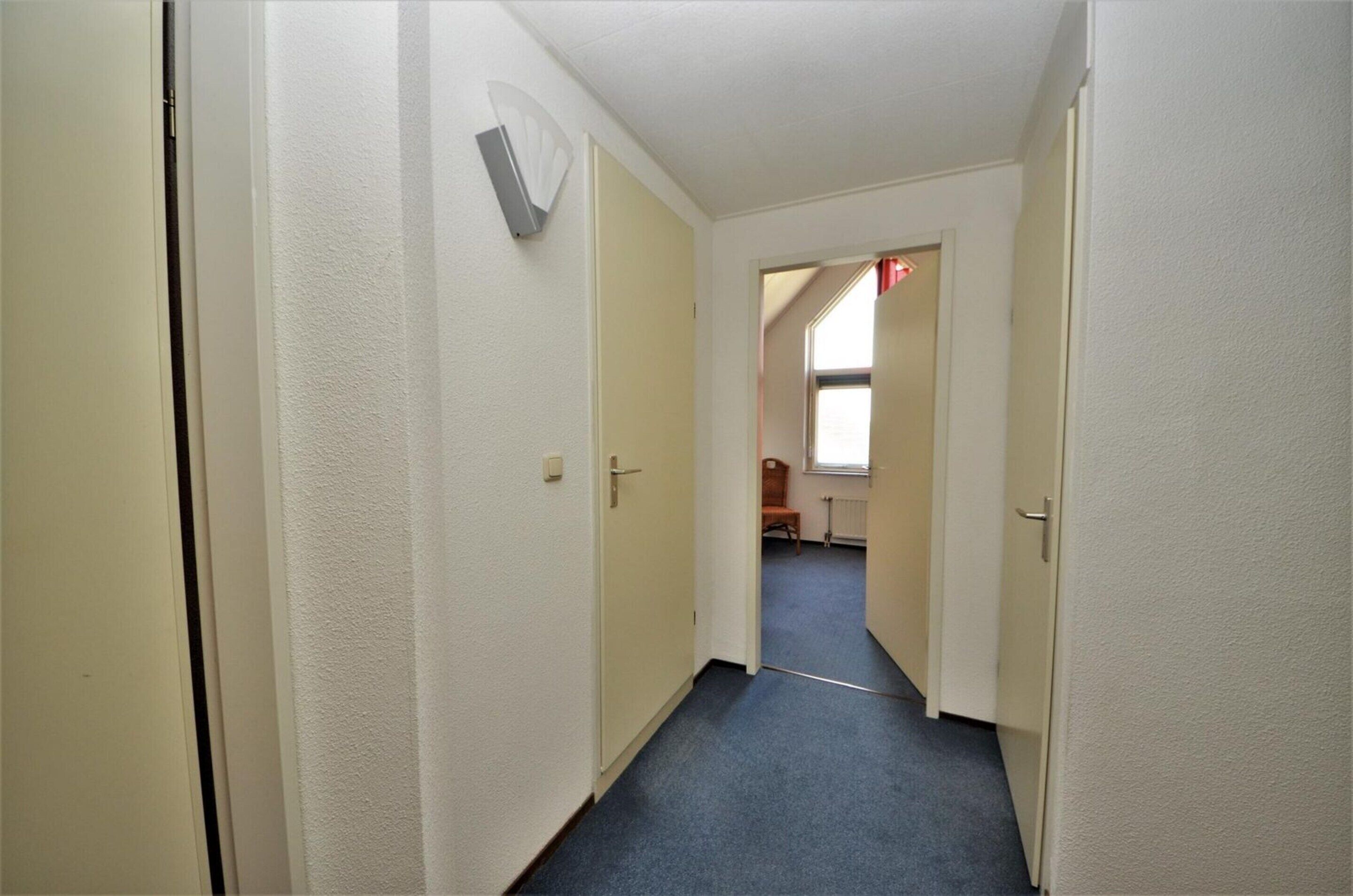 Ein schmaler Flur mit cremefarbenen Türen, einem blauen Teppich und einer weißen, strukturierten Wand.