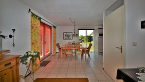 A dining area with a wooden table and chairs, a flower arrangement, and a view through a window with red blinds. - Lively Bungalow on the Water (Breskens)