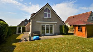 A two-story house with a large front porch, a sliding glass door, and a small attached garage. - Lively Bungalow on the Water (Breskens)