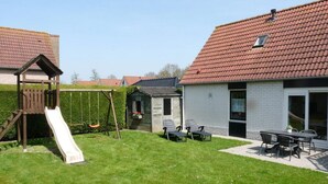 A backyard with a wooden swing set, a small shed, and a patio area with outdoor furniture. - Detached House Breskens Near Scenic Beaches (Breskens)