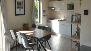 A modern kitchen with white cabinets, a stove, and a microwave. There is a dining area with a table and chairs. - Detached House Breskens Near Scenic Beaches (Breskens)