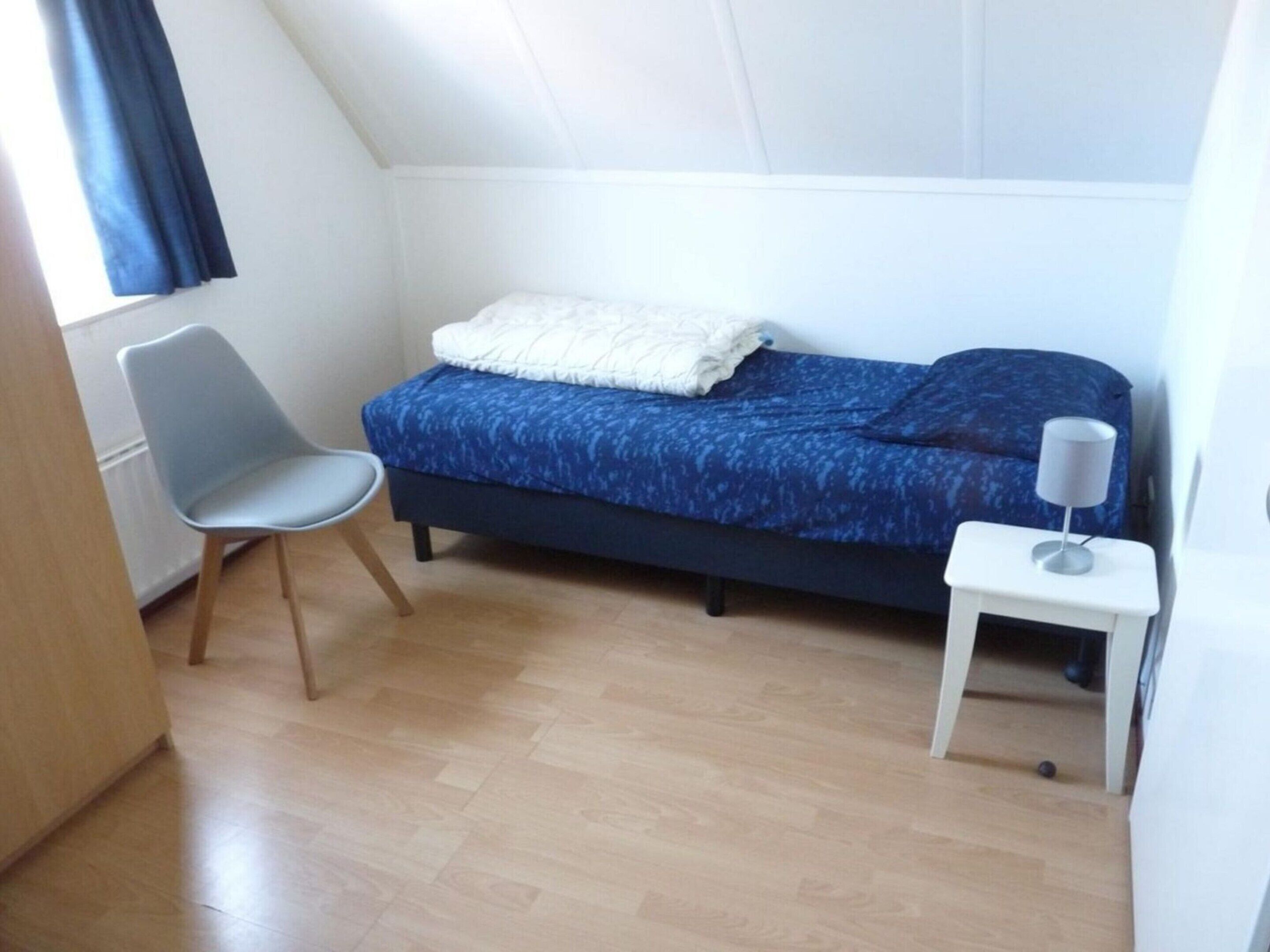 A small, neatly arranged bedroom with a bed, a chair, and a bedside table.
